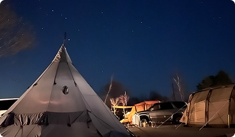星がきれいに見える夜空の下、形の違うテントが設置されているキャンプ場の写真