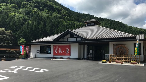 山と空を背景に和風の瓦屋根の建物と左側に水車の見える「道の駅万葉の里」