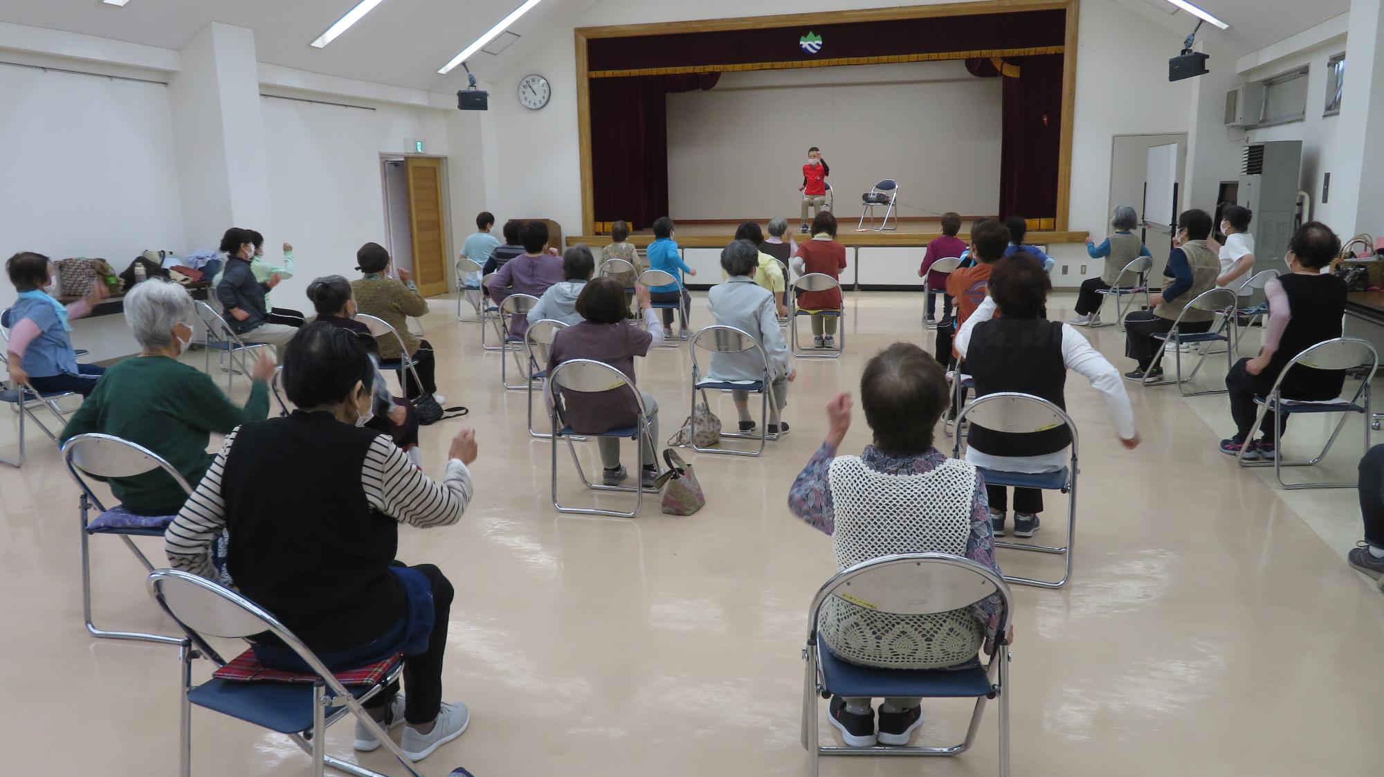 運動教室で高齢者が音楽に合わせて体操を行っているところ