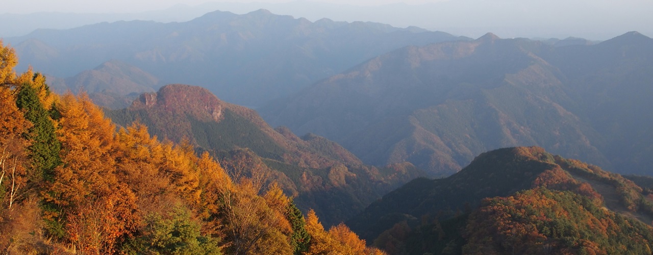 秋の夕暮れの西御荷鉾山から見える紅葉した山々