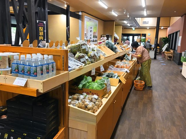 木製の棚に並べられた神流町産の野菜を見ている買い物中の女性